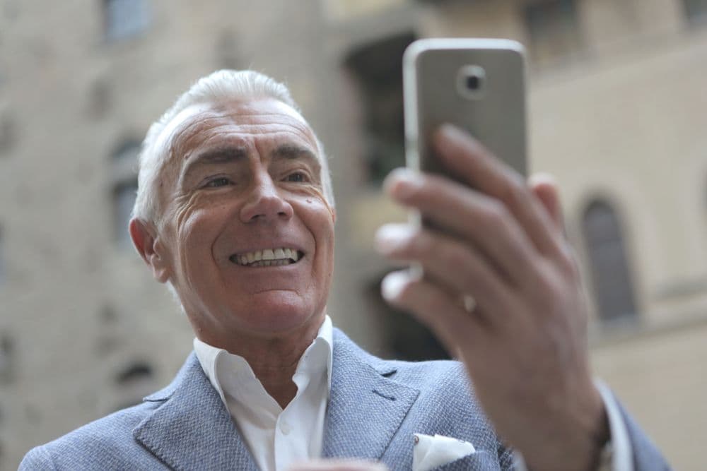 Mann mit grauem Haar schaut lächelnd auf sein Smartphone